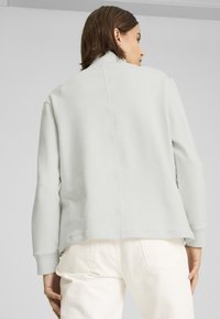 Sudadera gris claro con cuello alto, puños acanalados y corte recto. Textura suave, costuras mínimas, combinada con pantalones color off-white.