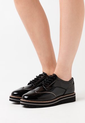 Chaussures à lacets en cuir verni noir avec des coutures contrastées et une semelle intermédiaire en liège texturé. Présentent une semelle extérieure en caoutchouc noir robuste.