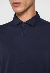 Marineblauw overhemd met knopen, met een gladde textuur, voorzien van een puntige kraag en twee knopen bij de hals, gemaakt van lichtgewicht stof.