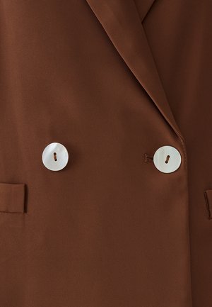 Rjav blazer z gladko teksturo, dvogumbni dizajn in dvema velikima belima gumboma. Ima krojene reverje in stranske žepe.