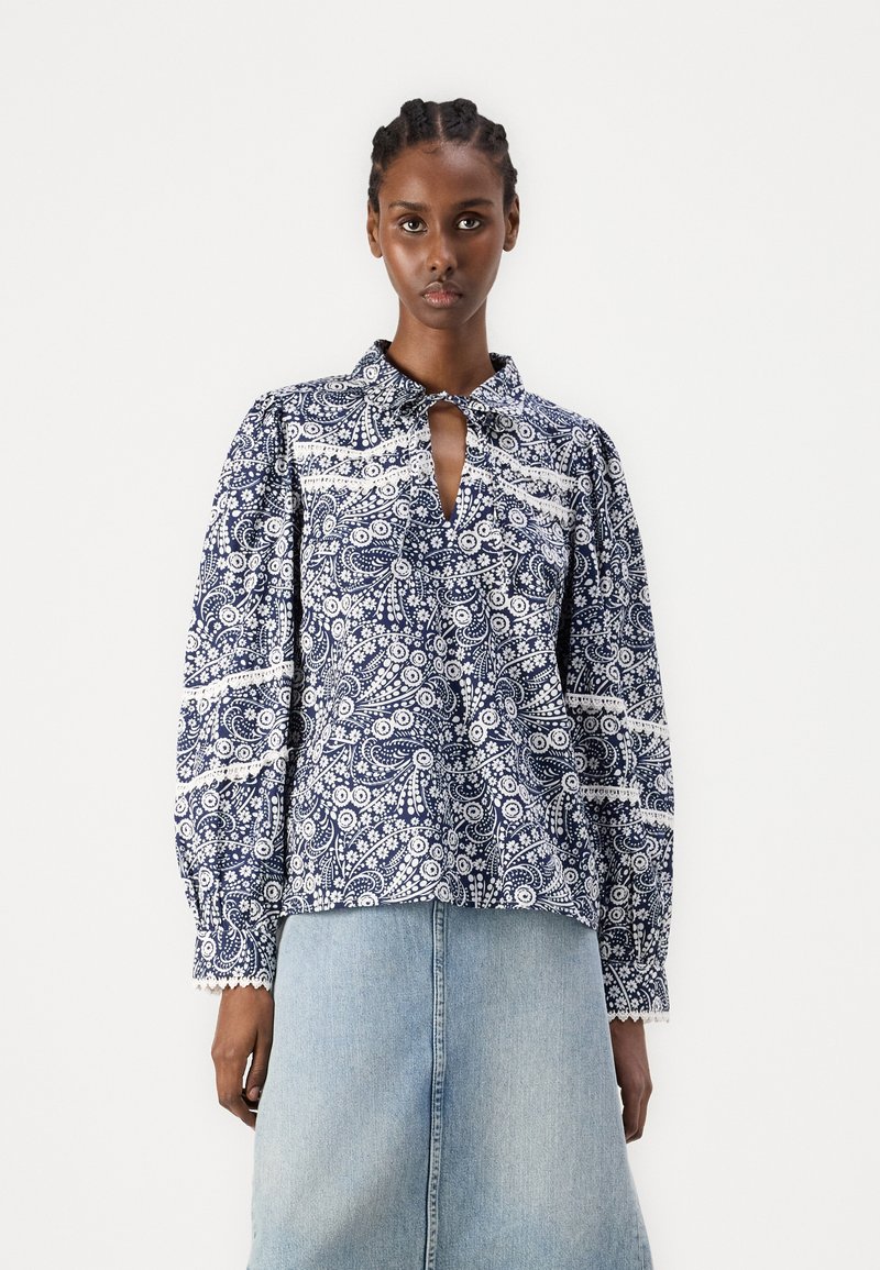 Løsgående marineblå bluse med hvitt blomsterdesign, kragehals og nøkkelhullsdetalj foran. Lange puffermer og blondekant.