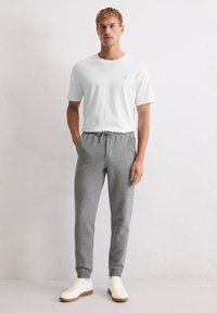 Biała bawełniana koszulka z okrągłym dekoltem, w połączeniu z szarymi joggerami z polaru, wyposażonymi w ściągacz z sznurkiem w pasie oraz elastyczne mankiety. Białe trampki.