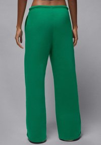 Zielone spodnie dresowe o szerokich nogawkach, miękkiej teksturze, z elastycznym pasem i bocznymi kieszeniami, pokazane od tyłu na szarym tle.