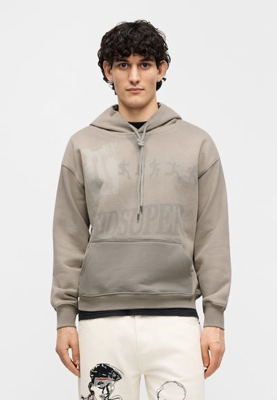 Φούτερ με κουκούλα σε απαλό μπεζ χρώμα, με γραφικό τύπωμα και κορδόνι. Μαλακή υφή με εμπρόσθια τσέπη. Εμφανές λογότυπο "KIDSUPER".