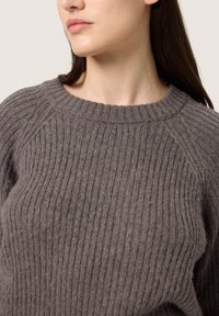 Gray ribbed sweater with a round neckline and raglan sleeves, made from a soft knit material. Features a textured surface with subtle variations.