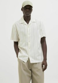 Chemise à manches courtes, à col, de couleur crème avec des rayures verticales beige clair. Comprend des boutons et une coupe décontractée. Associée à un pantalon beige.