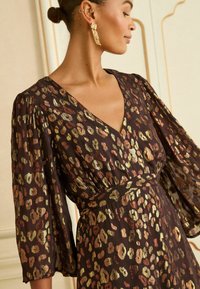 Rochie maro cu model, cu decolteu în V și mâneci bufante și fluide. Materialul are un imprimeu leopard metalic în nuanțe pământii.