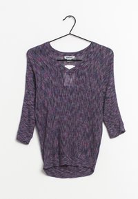 Pull-over en V tricoté violet, noir et rose avec des manches trois-quarts suspendu sur un cintre noir, sur un fond blanc.