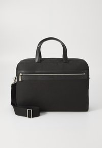 Sac en tissu noir avec des accents en cuir, doté d'une poignée supérieure, d'une bandoulière détachable, d'une poche zippée à l'avant et d'une forme rectangulaire.