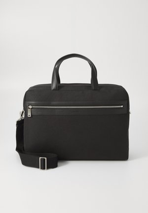 Zwarte stoffen tas met leren accenten, voorzien van een handvat aan de bovenkant, een afneembare schouderriem, een voorste ritszak en een rechthoekige vorm.