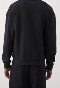 Felpa nera con colletto rotondo, polsini e fondo a coste. Realizzata in materiale morbido; presenta un design semplice e non decorato.