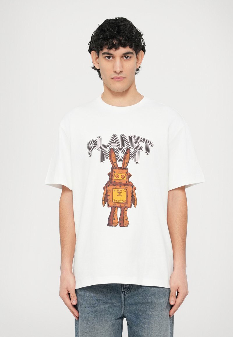 Άσπρο βαμβακερό μπλουζάκι με μεγάλο γραφικό τύπωμα ενός καφέ ρομπότ που μοιάζει με λαγό, με κίτρινο τετράγωνο σώμα και το κείμενο "PLANET MCM."