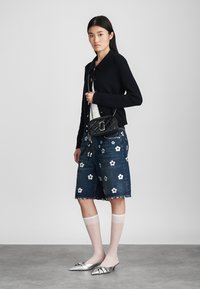 Cardigan negru cu dungi, top alb, pantaloni Bermuda din denim cu broderie florală, pantofi plata argintii cu vârf ascuțit și șosete albe până la genunchi. Geantă crossbody neagră.