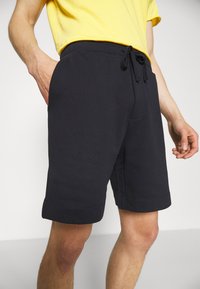 Shorts en coton bleu marine foncé avec une taille élastique et un cordon de serrage, dotés de poches latérales et d'une coupe décontractée, se terminant au-dessus du genou.