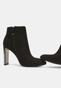 Stivaletti in suede nero con punta a punta e tacco metallico di 10 cm; presentano una cerniera laterale e una texture liscia.