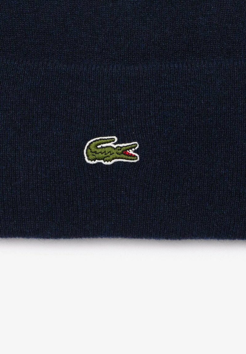 Bonnet en tricot bleu marine avec une texture côtelée, arborant un petit logo de crocodile vert brodé avec des accents rouges sur le côté.