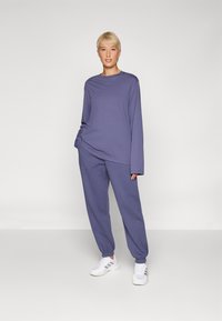 Lilla langermet topp med avslappet passform, kombinert med matchende tapered joggebukser. Begge plaggene har myk stoff og elastiske mansjetter.