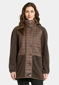 Bruine bovenkleding met een gequiltte textuur op de bovenste helft en zachte fleece op de onderste helft, voorzien van een hoge kraag en drukknoopsluiting.