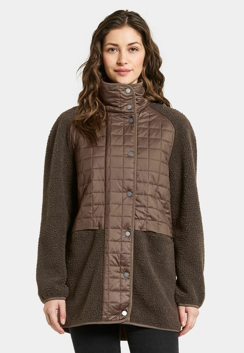 Bruine bovenkleding met een gequiltte textuur op de bovenste helft en zachte fleece op de onderste helft, voorzien van een hoge kraag en drukknoopsluiting.