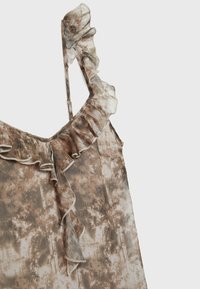 Haut sans manches à motifs marron et crème avec un col à volants et de fines bretelles en tissu léger et transparent.