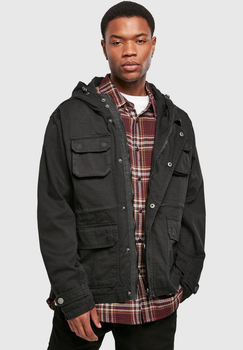 Black hooded jacket with multiple pockets, button accent, and a zip closure, layered over a red and black plaid shirt. Smooth texture.