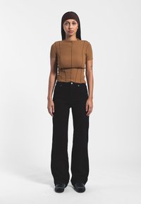 Top corto de punto acanalado marrón con detalles de costura, combinado con unos pantalones vaqueros de pierna ancha negros de cintura alta y zapatos negros con acentos azules.