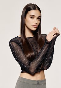 Top lungo trasparente nero con motivo a pois argento, design aderente e lunghezza corta, abbinato a pantaloni grigi chiari a vita alta.