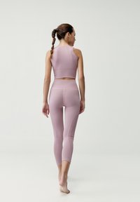 Jasnoróżowy zestaw odzieży sportowej składający się z dopasowanego, bezrękawnikowego topu i legginsów o wysokim stanie z żebrową teksturą i detalami szwów.