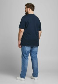 Marineblaudes Baumwoll-T-Shirt mit klassischer Passform, kurzen Ärmeln und rundem Ausschnitt, kombiniert mit hellblauen Jeans und weißen Turnschuhen.