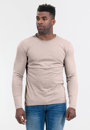 T-shirt beige a maniche lunghe con scollatura rotonda, realizzato in tessuto morbido, abbinato a jeans in denim blu. Design semplice, con minimalismo nei dettagli.