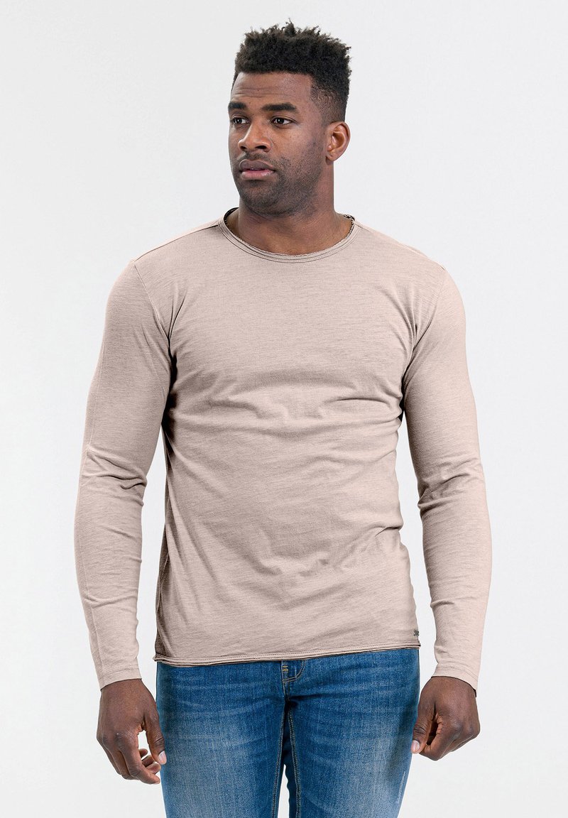 Beige t-shirt met lange mouwen en een ronde hals, gemaakt van zachte stof, gecombineerd met blauwe denim jeans. Eenvoudig ontwerp, minimale detailing.