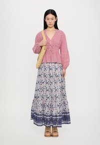 Rot gestreifte Bluse mit V-Ausschnitt und geraffter Taille, kombiniert mit einem floralem Maxikleid mit blauen und pinken Mustern sowie einem marineblauen Saum. Gewebte Tragetasche.