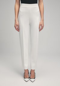 Witte op maat gemaakte broeken met een hoge taille, voorzien van een gladde textuur en een geplooide voorkant, gecombineerd met zwart-witte puntige hakken.