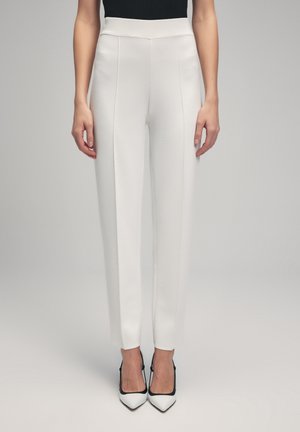 White tailored trousers with a high waistband, featuring a smooth texture and creased front, paired with black and white pointed heels.