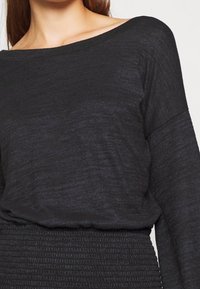 Dark gray long-sleeve top made of a soft, textured fabric. Features a boat neckline and a relaxed fit with distinct horizontal patterns.