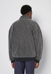 Grau meliertes Fleecejacke mit hohem Kragen, übergroßer Passform und gerippten Bündchen. Entworfen mit einem subtilen, melierten Muster für zusätzliche Wärme.