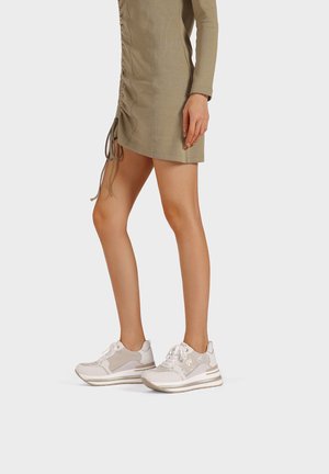 Sneaker atletici bianchi con accenti grigio chiaro, dotati di una tomaia texturizzata, suola liscia e lacci. Indossati con un vestito aderente verde oliva.
