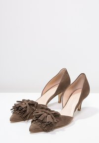Une paire de chaussures pour femmes en suède marron à talons bas, avec des bouts pointus et de grandes franges décoratives à l'avant.