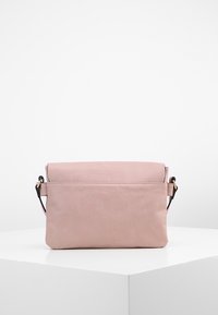 Borsa a tracolla in pelle rosa chiaro con chiusura a pattina e accessori in metallo neri, esposta su un pedistallo geometrico bianco.