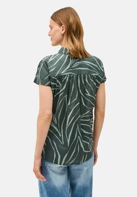 Camicia a maniche corte in tessuto verde scuro con un motivo a foglia in verde chiaro, dotata di una schiena plissettata e colletto. Design dal taglio casual.