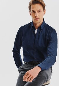 Ciemnoniebieska koszula zapinana na guziki z teksturowanej tkaniny, z długimi rękawami i kołnierzykiem, zestawiona z szarymi spodniami. Prosty design, dopasowany krój.