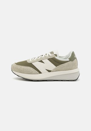 Zapatillas con una combinación de colores verde y beige, materiales de ante y malla, franjas laterales blancas y una suela gruesa y acolchada.