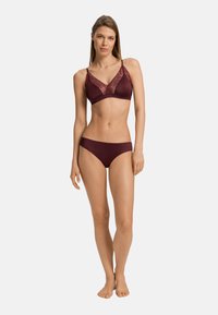 Bralette color bordeaux con rifiniture in pizzo, spalline regolabili e slip coordinato, texture liscia, forma definita e design minimalista.