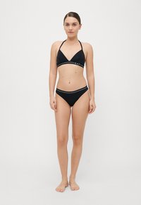 Melnas bikini komplekts ar trīsstūra formu augšdaļu un zemu jostasvietu, abām daļām ir kontrastējoši balti akcenti un logotipa detaļa. Gluda auduma tekstūra.