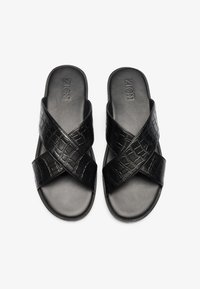 Sandales de plage noires à enfiler, avec une tige en faux cuir texturé, une semelle intérieure lisse et une semelle extérieure durable. Présente un logo de marque discret sur le dessus.