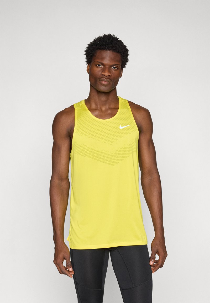 Gul Nike tank topp med et teksturert geometrisk mønster i den øvre delen og rund hals, parret med svarte treningslegger.
