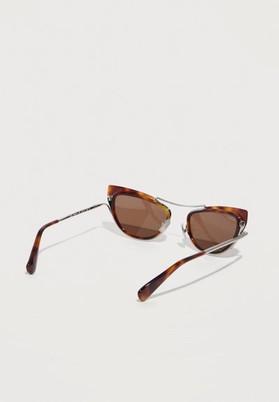 Γυαλιά ηλίου με σκελετό σε σχήμα γάτας με μοτίβο χελώνας, καφετί φακούς και ασημένιες μεταλλικές λεπτομέρειες, τοποθετημένα σε λευκή επιφάνεια.