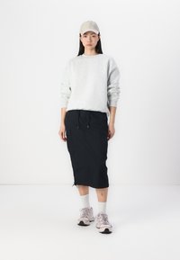 Lichtgrijze sweatshirt, zwarte midi-rok met cargozakken, beige pet en lichtroze sneakers met witte sokken. Eenvoudige en praktische outfit.