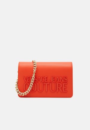 Mała prostokątna czerwona torebka z wytłoczonym napisem "Versace Jeans Couture" oraz krótkim złotym łańcuszkiem, na jednolitym tle.