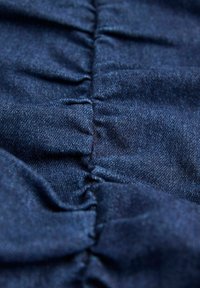 Gros plan d'un tissu denim bleu foncé avec une couture élastique froncée créant des plis horizontaux texturés.